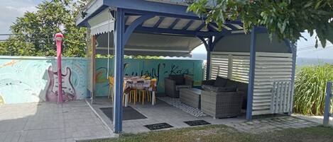 A covered outdoor seating area with a table and chairs, a pink flamingo decoration, and a mural on the wall.