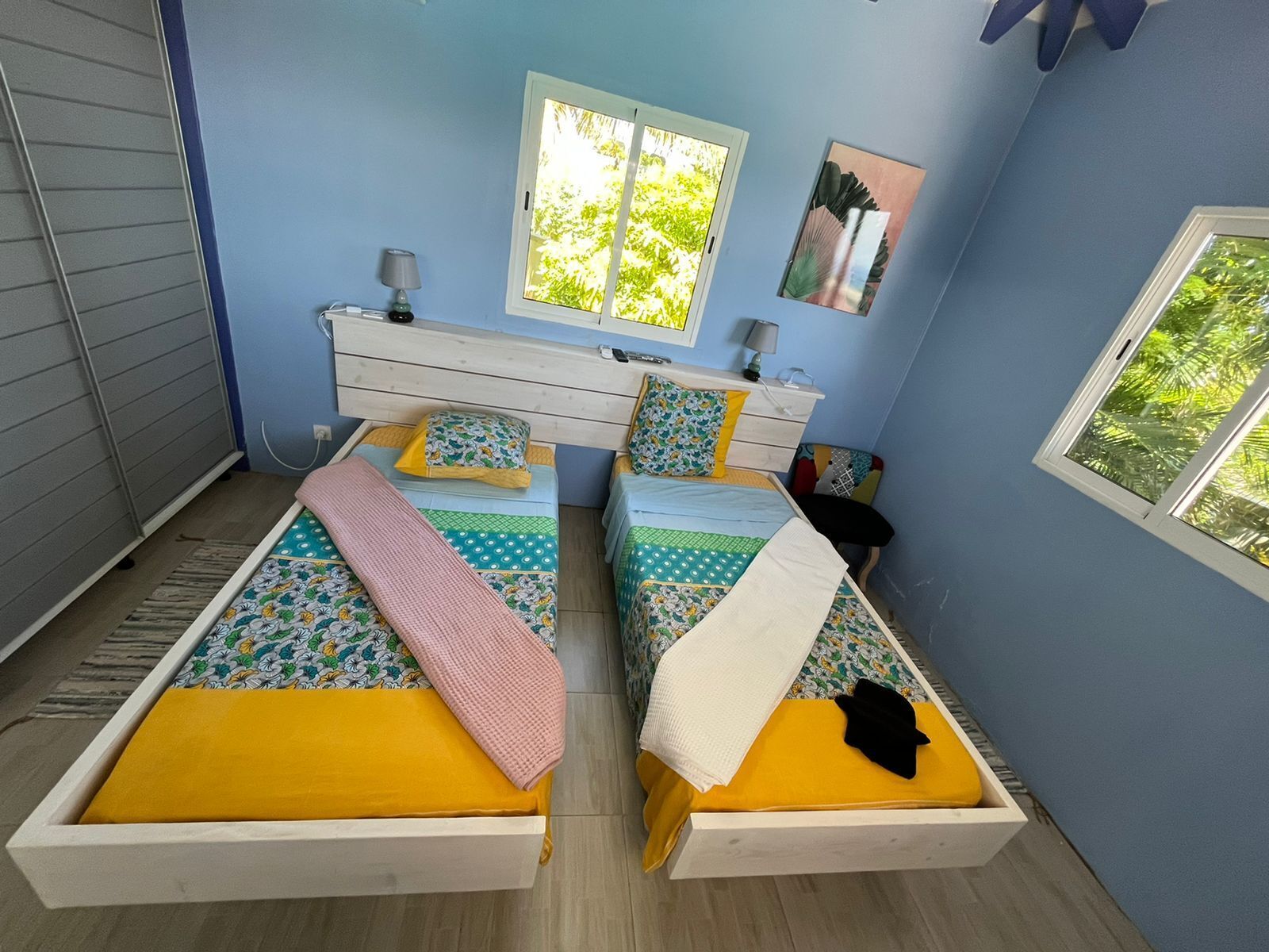 A bedroom with two beds, a dresser, two lamps, and two windows.