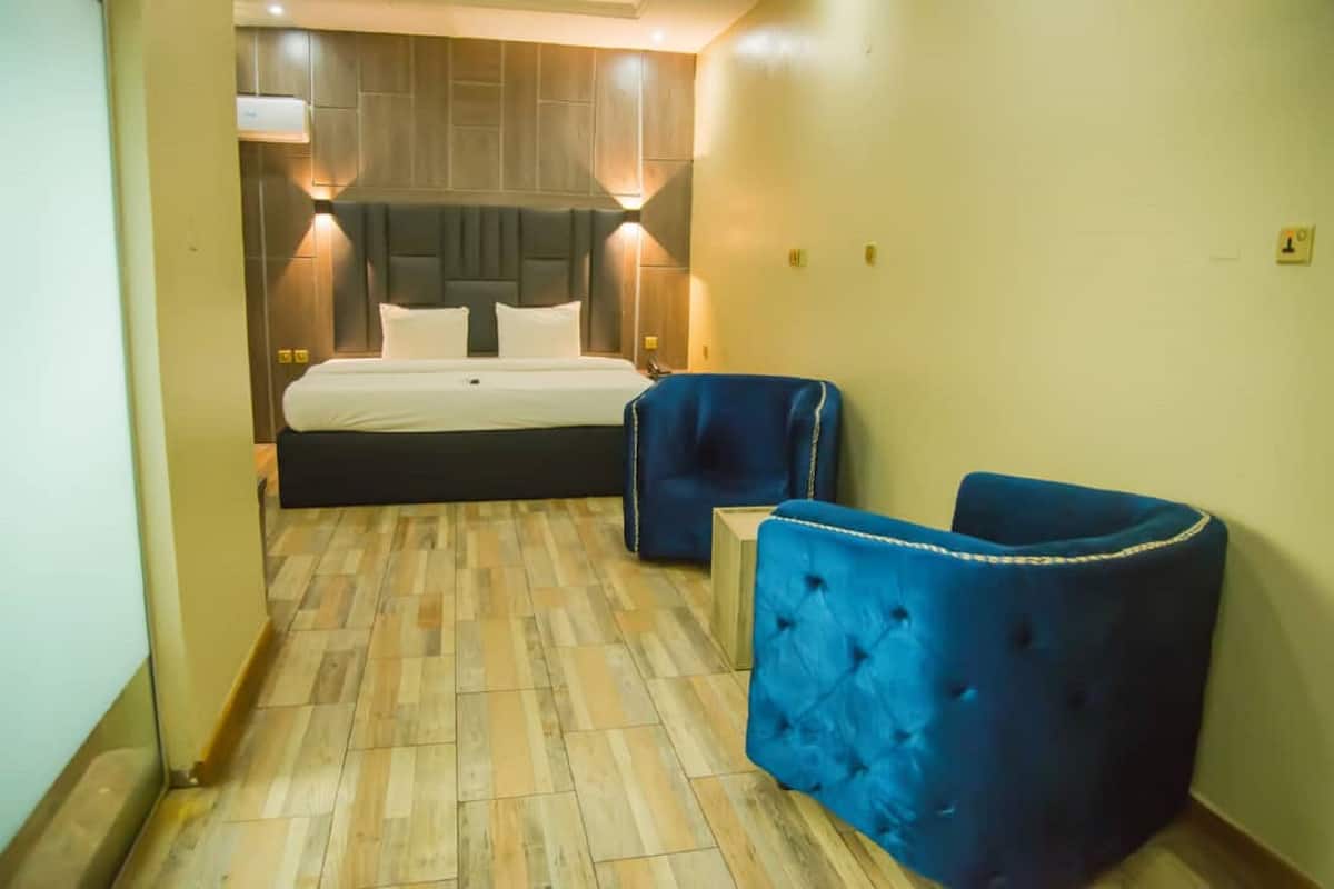 Una habitación de hotel con una cama grande, dos sillones azules y suelo de madera.