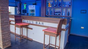 Zona de bar con dos taburetes de mimbre, una barra con un letrero de neón y una exhibición de botellas de licor.