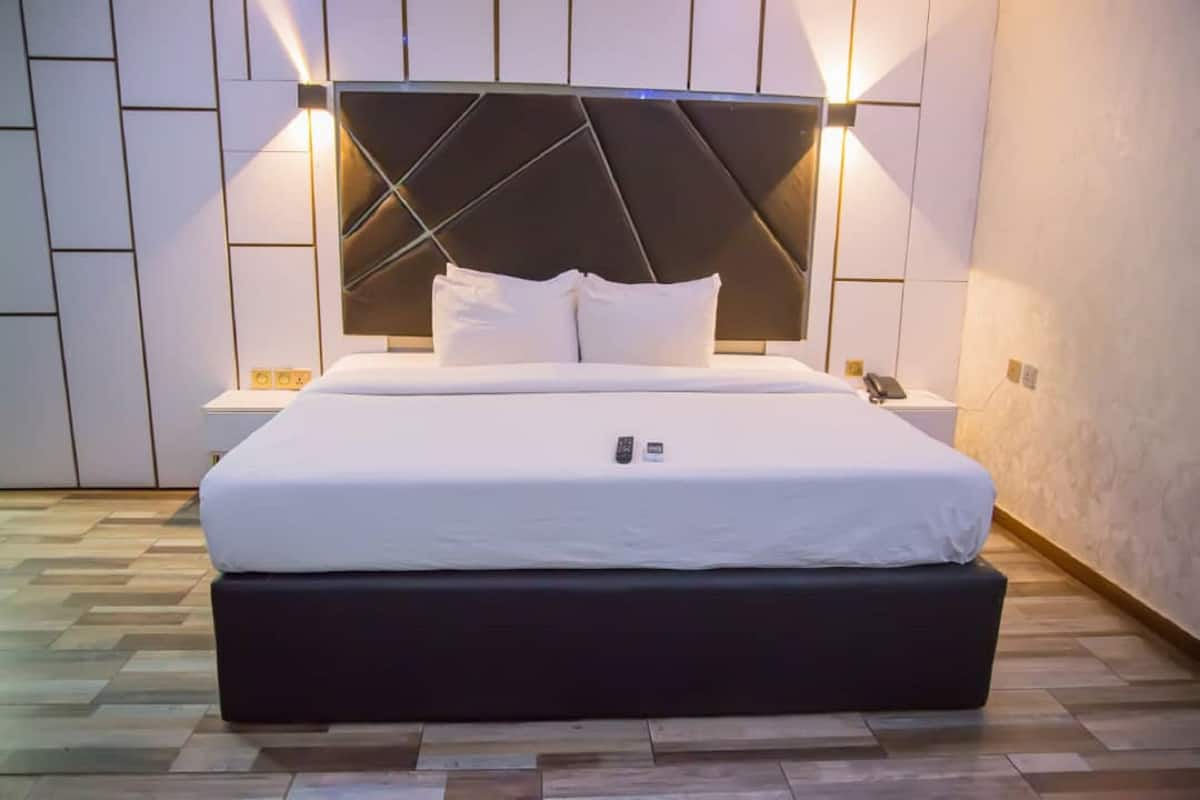 Una habitación de hotel moderna con una cama grande, cabecera con iluminación integrada, mesitas de noche y suelo de madera.