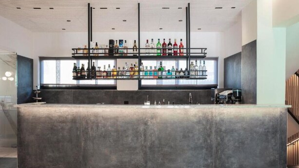A modern bar area with a concrete counter, multiple shelves of liquor bottles, and a clean, minimalist design. - Moon Palace Hotel  (Arese)
