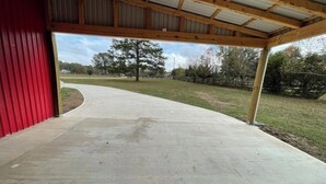 A covered patio area with a concrete walkway leading to a grassy field. - Country Oasis Room - A (Hockley)