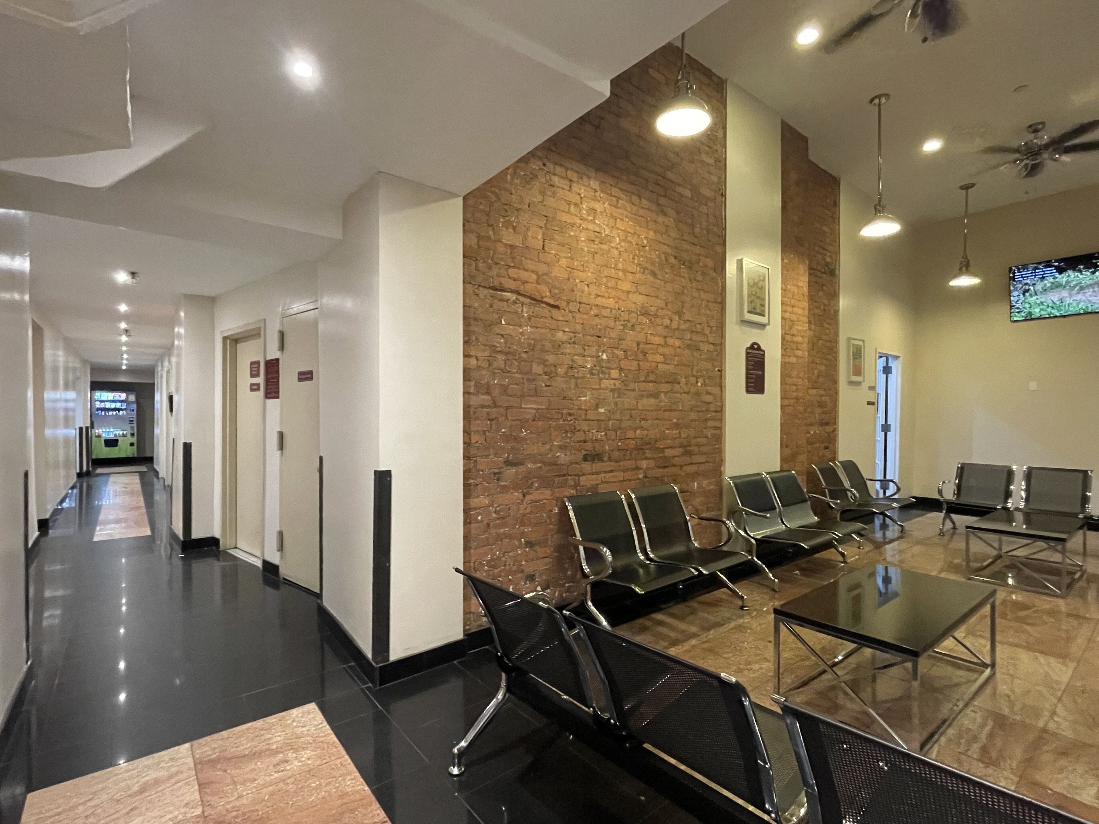 A modern waiting area with a long corridor, a brick accent wall, and several seating areas with tables.