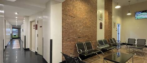 A modern waiting area with a long corridor, a brick accent wall, and several seating areas with tables.