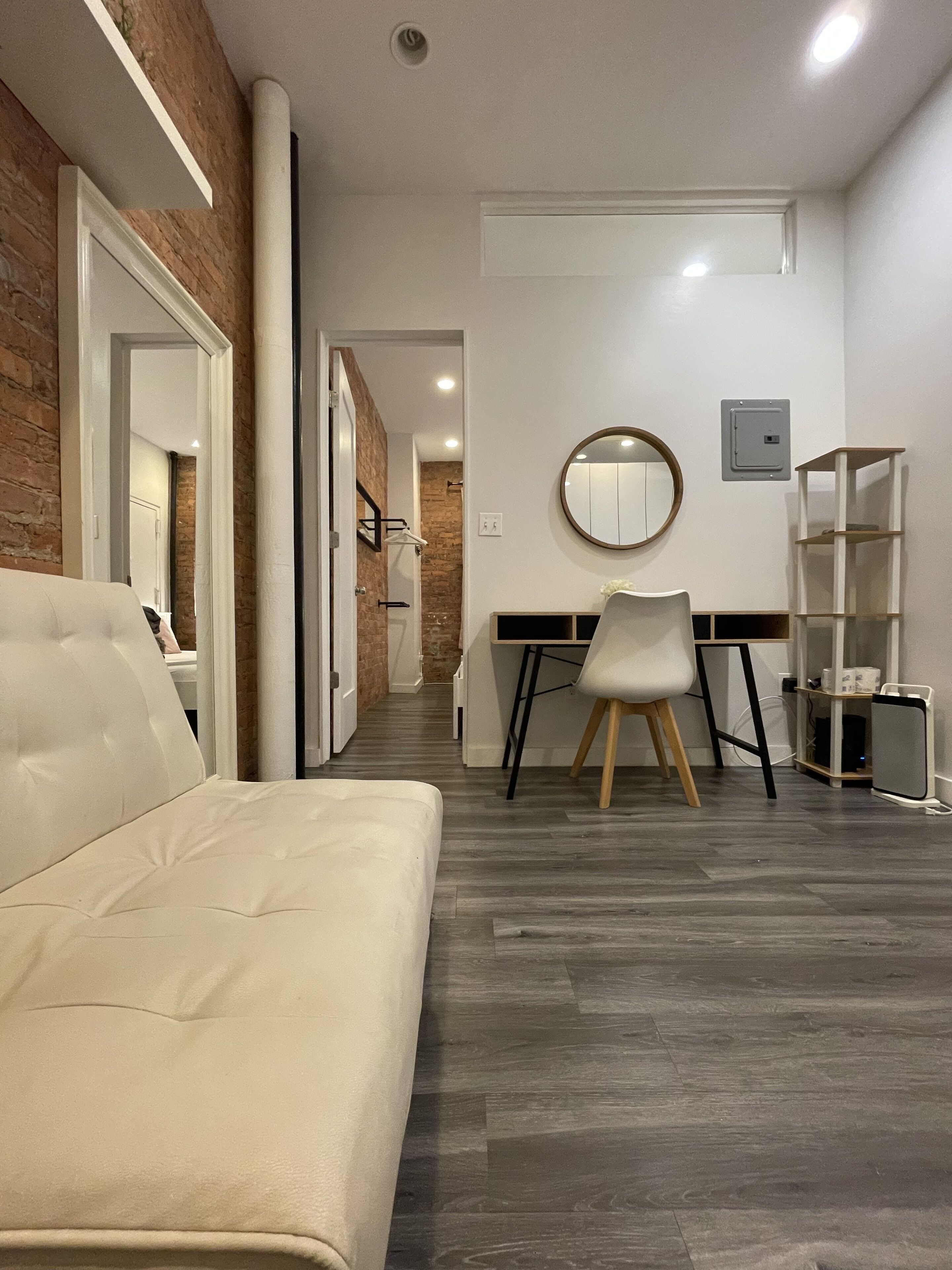 A modern room with a white sofa, a desk with a chair, a round mirror, and a bookshelf.
