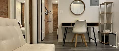 A modern room with a white sofa, a desk with a chair, a round mirror, and a bookshelf.