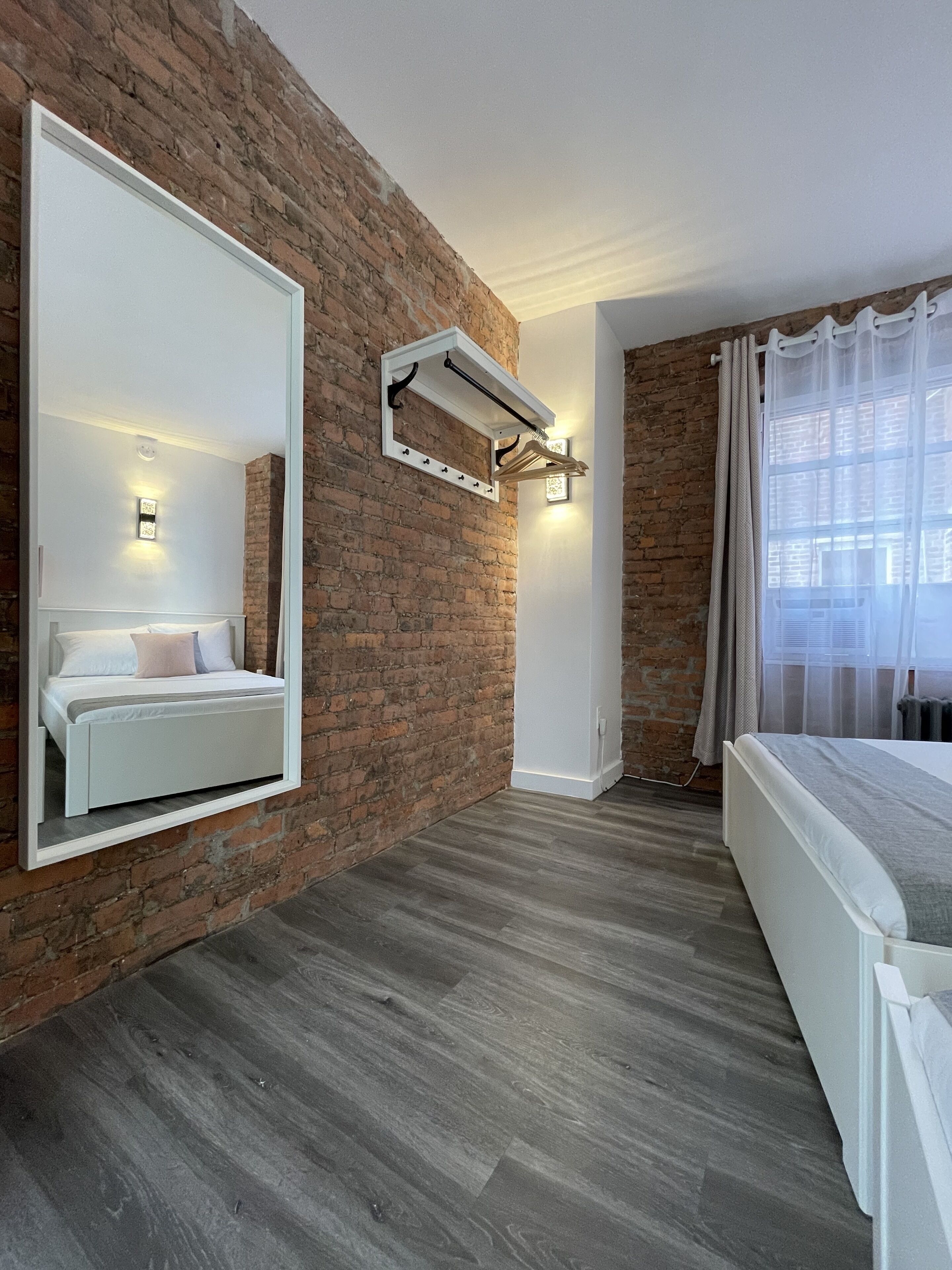 A modern bedroom with a brick wall, a large mirror, a bed, and a built-in light fixture.