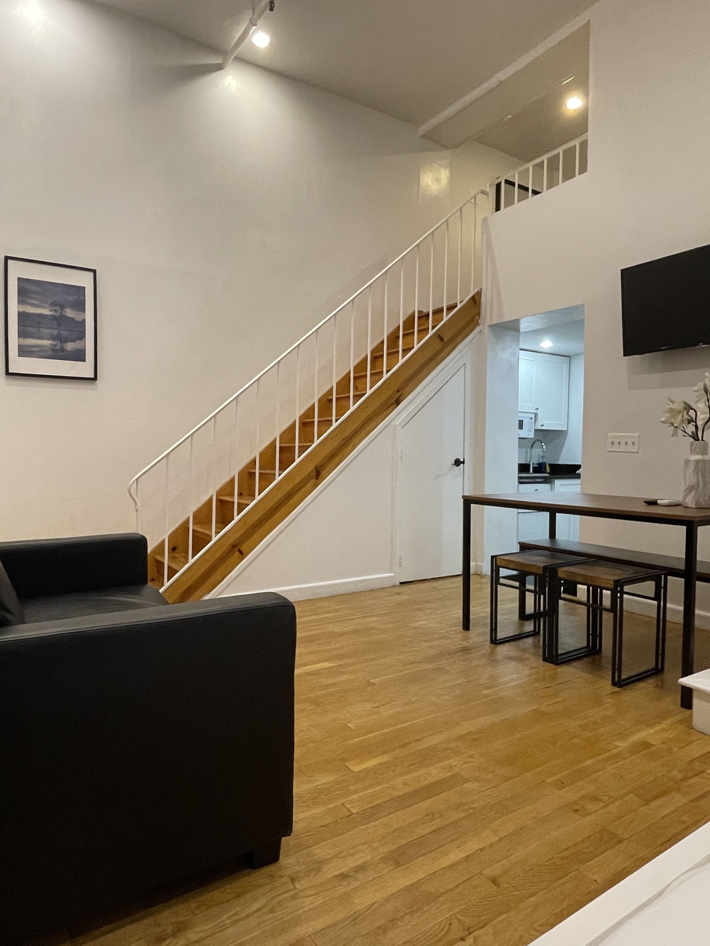 Una sala de estar moderna con una escalera de madera, un comedor con mesa y bancos, y una cocina al fondo.