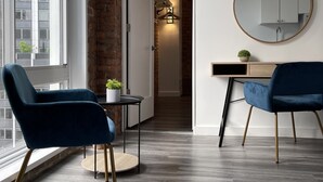 Een moderne woonkamer met twee blauwe stoelen, een ronde spiegel en een kleine tafel met een plant.