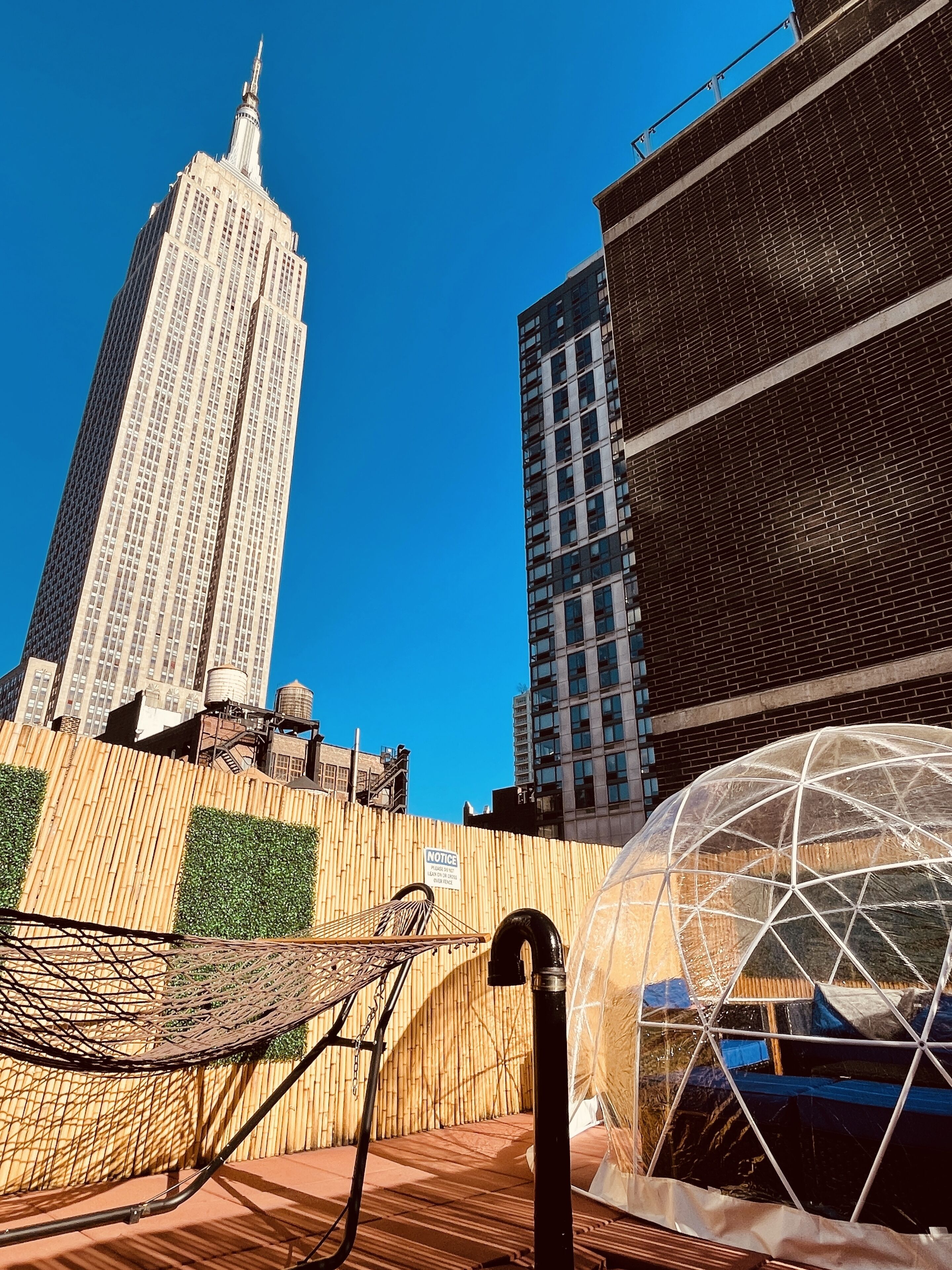 A rooftop terrace with a view of the Empire State Building, a metal chair, and a geodesic dome structure.