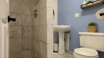 Un baño con ducha, lavamanos, inodoro y un estante con artículos de aseo.