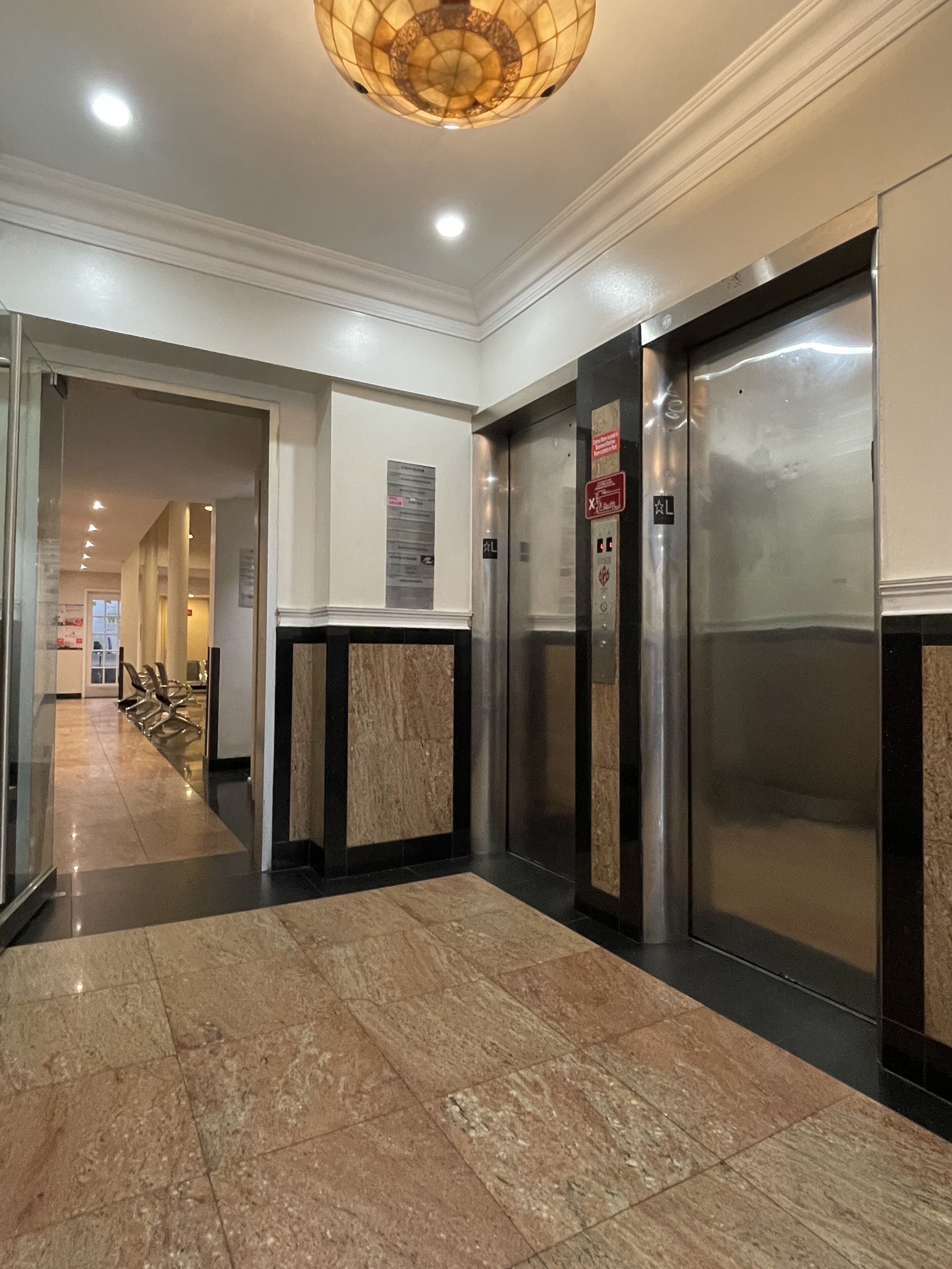 A modern elevator area with marble flooring, a glass partition, and a ceiling light fixture.
