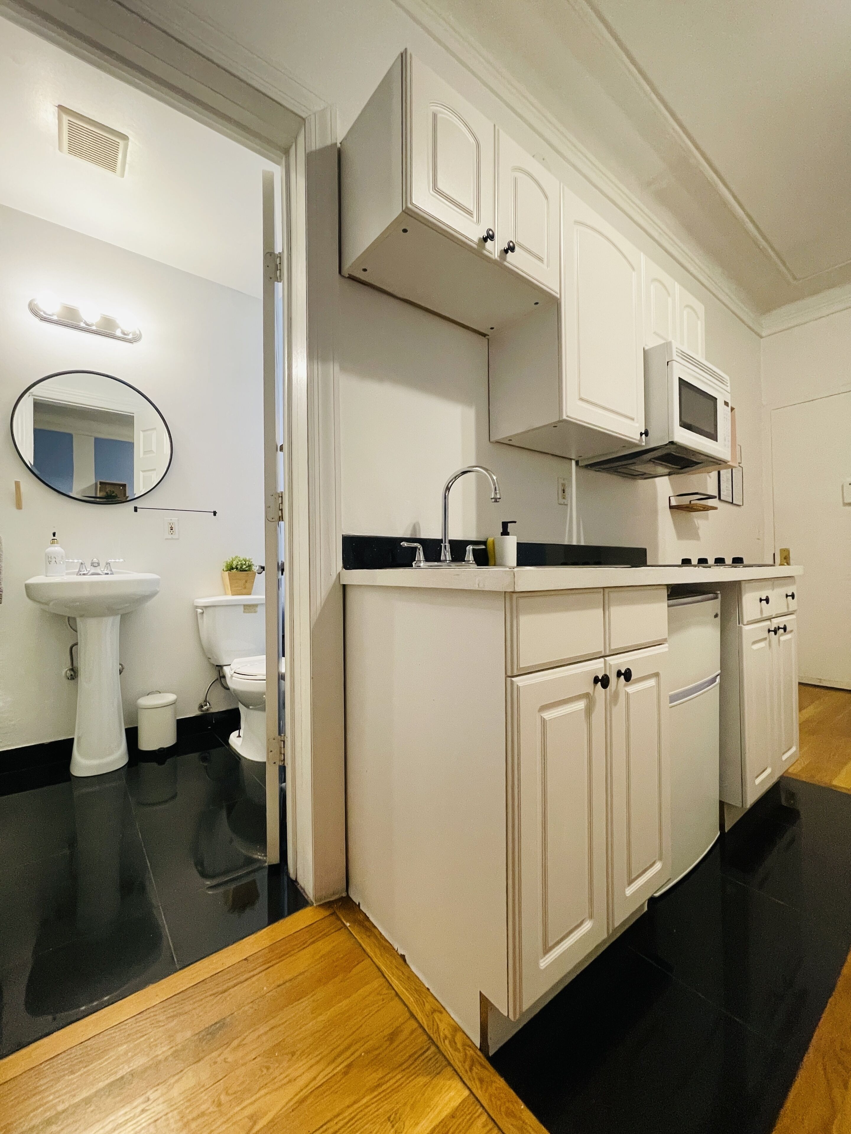 A modern kitchen with white cabinets, a black countertop, a sink, a microwave, and a wooden floor.