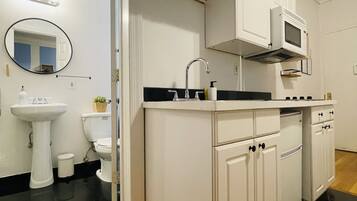 Una cocina moderna con armarios blancos, encimera negra, un lavabo, microondas y suelo de madera.