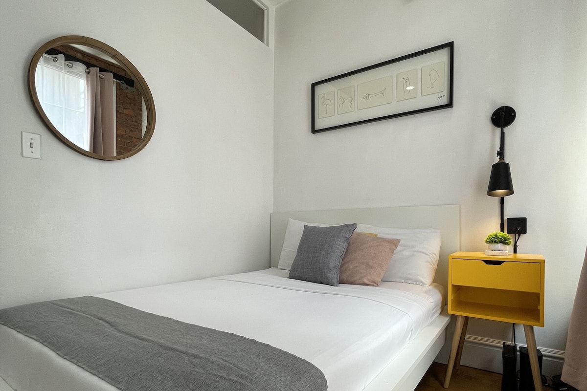 A bedroom with a bed, a bedside table, a lamp, a mirror, and a framed picture on the wall.