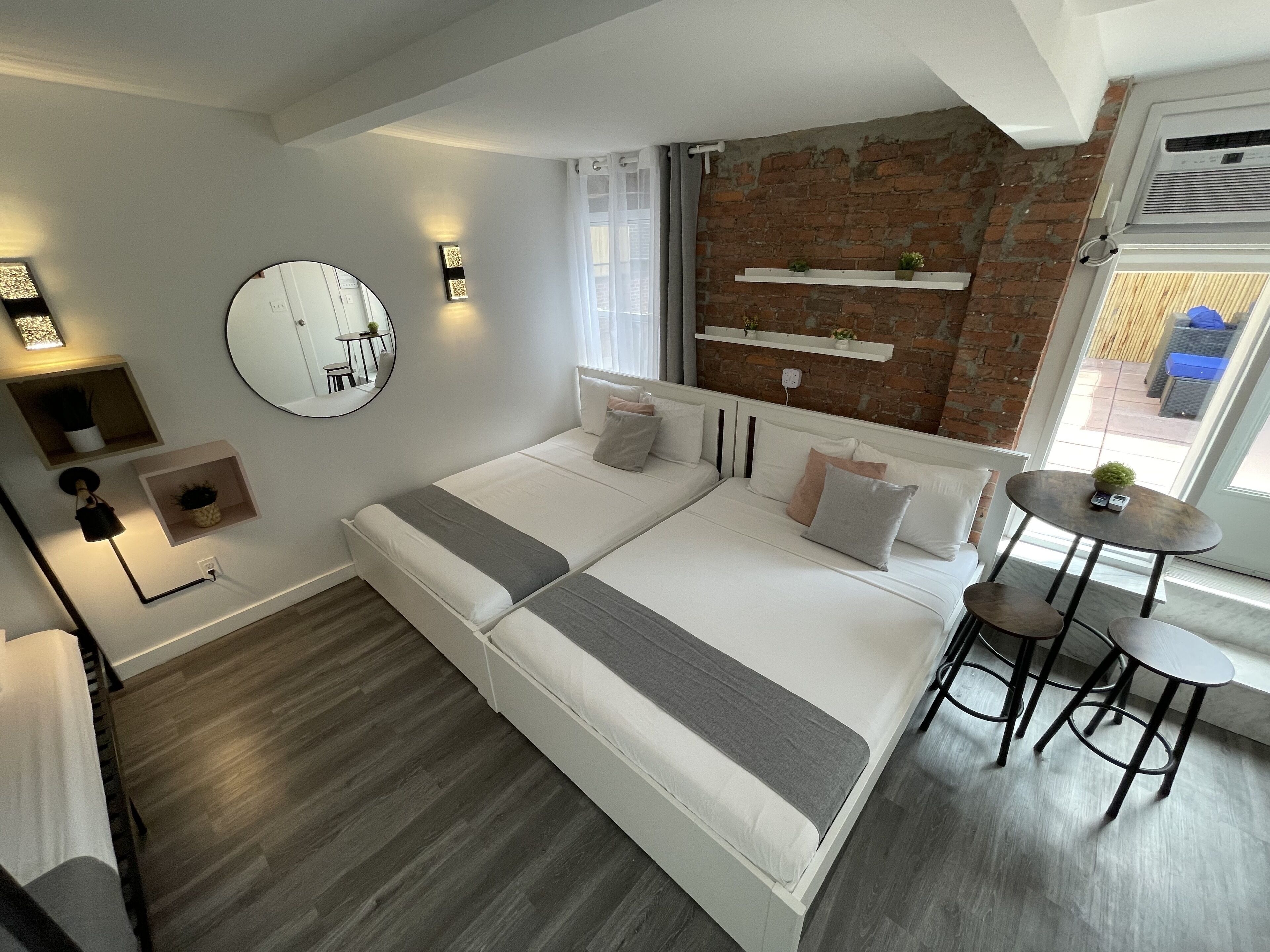 Ein modernes Schlafzimmer mit einem großen Bett, Nachttischen, einem runden Spiegel und einer Ziegelwand.