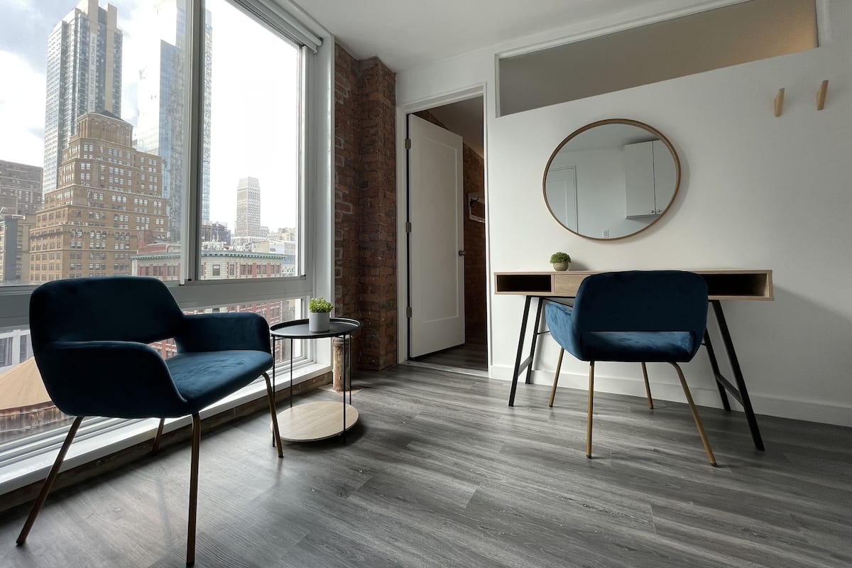 A modern room with a large window, two blue chairs, a round mirror, and a desk.