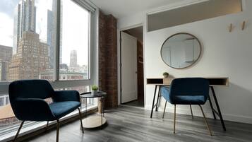 A modern room with a large window, two blue chairs, a round mirror, and a desk.