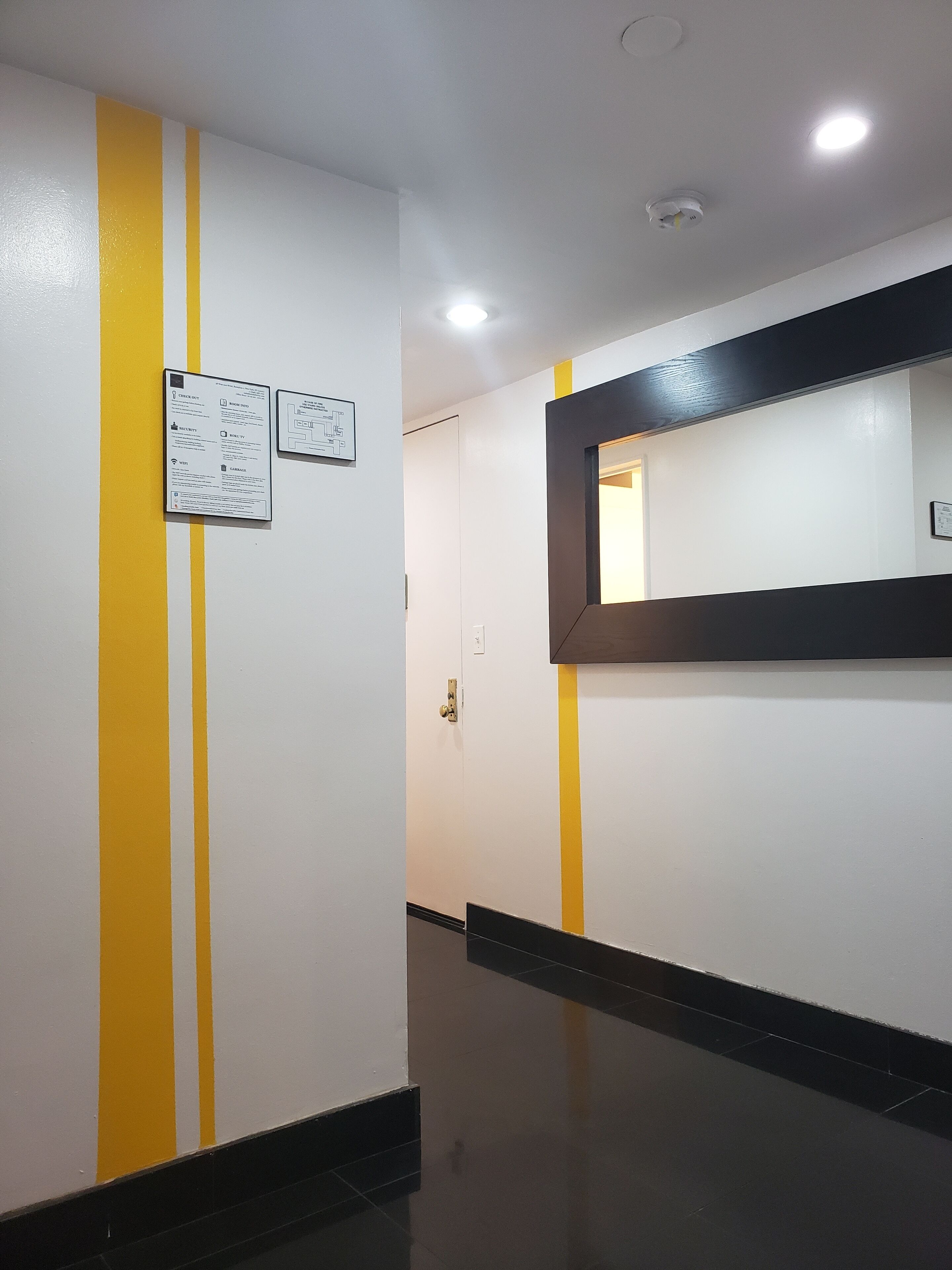 A hallway with yellow stripes on the walls, a black-tiled floor, and a ceiling light.