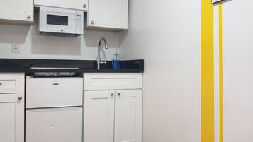 A kitchen with white cabinets, a microwave, a refrigerator, and a sink.