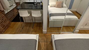 Une chambre d’hôtel compacte comprenant un coin cuisine, un petit espace repas et un lit avec une tête de lit grise.