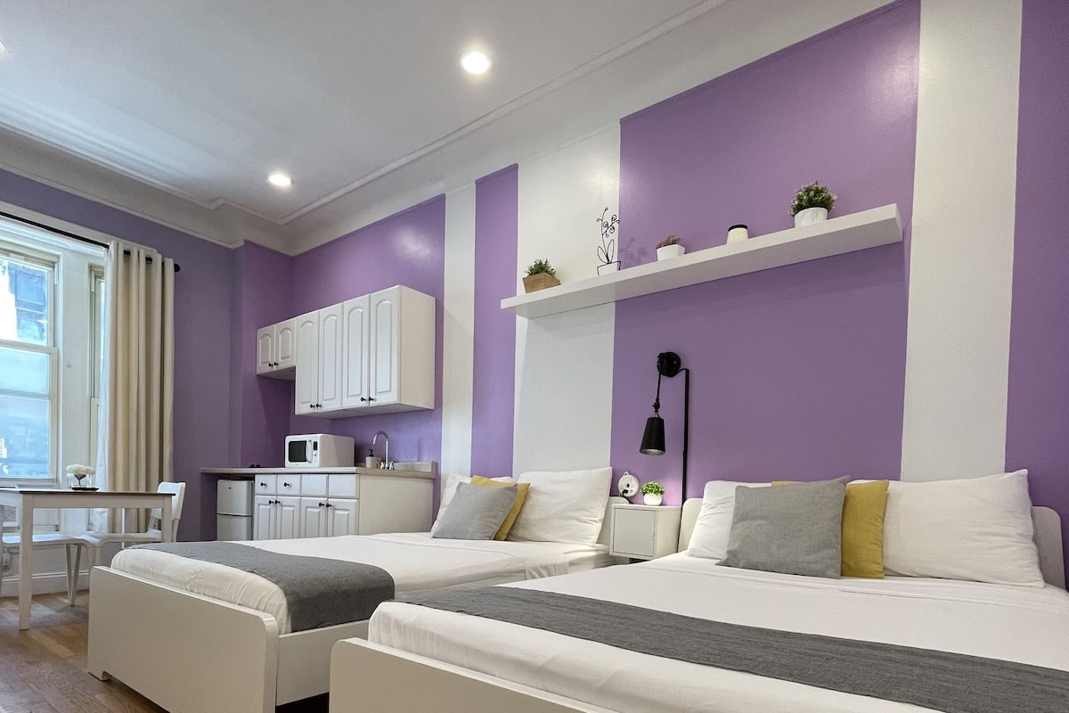 A modern bedroom with a large bed, a desk, and a kitchenette.