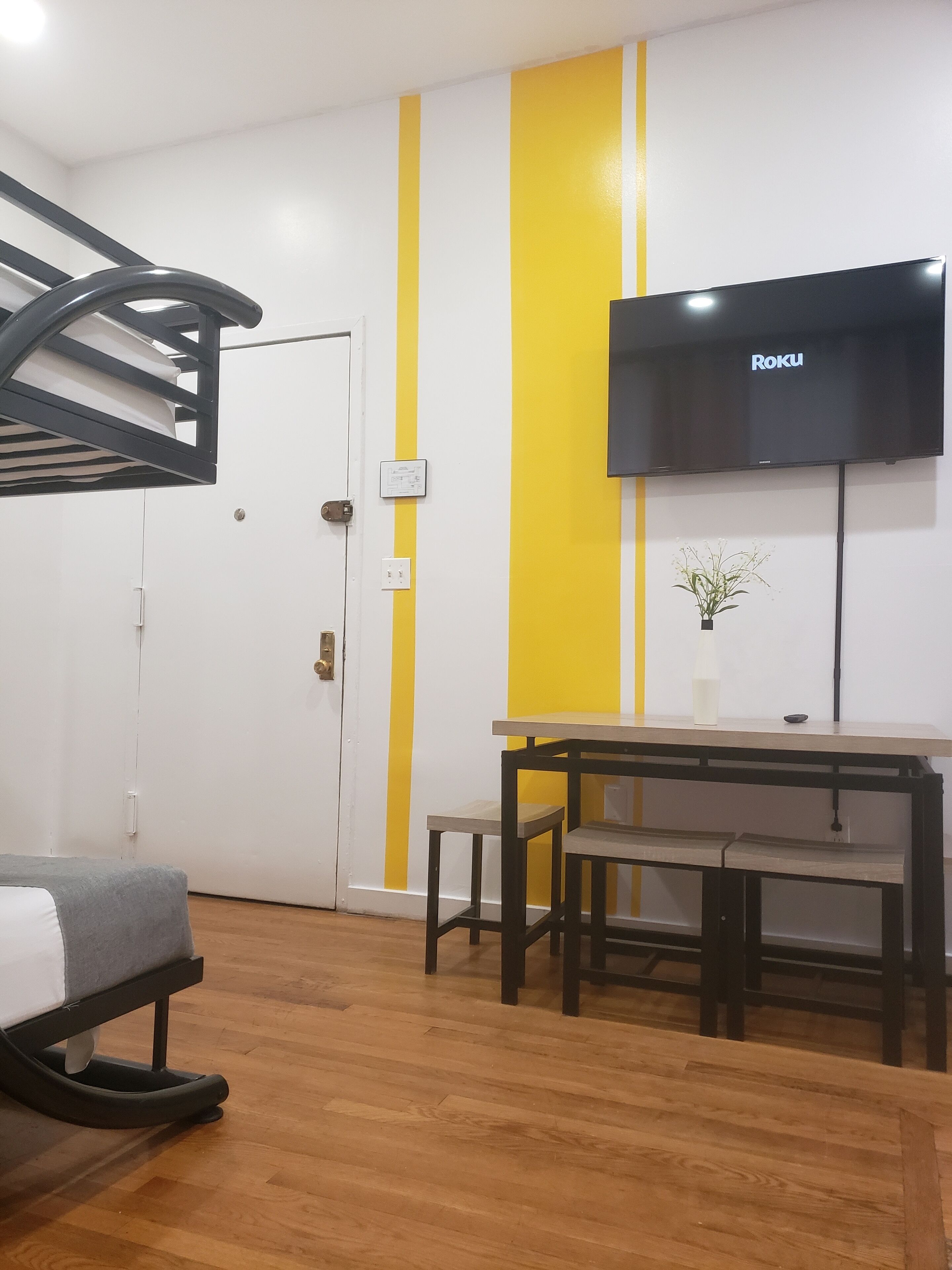 A room with a bunk bed, a desk with a chair, a flat-screen TV mounted on the wall, and a small potted plant on the desk.