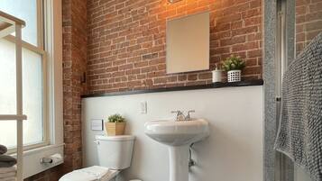 Un bagno con parete in mattoni, un water bianco, un lavabo su piedistallo e uno specchio.