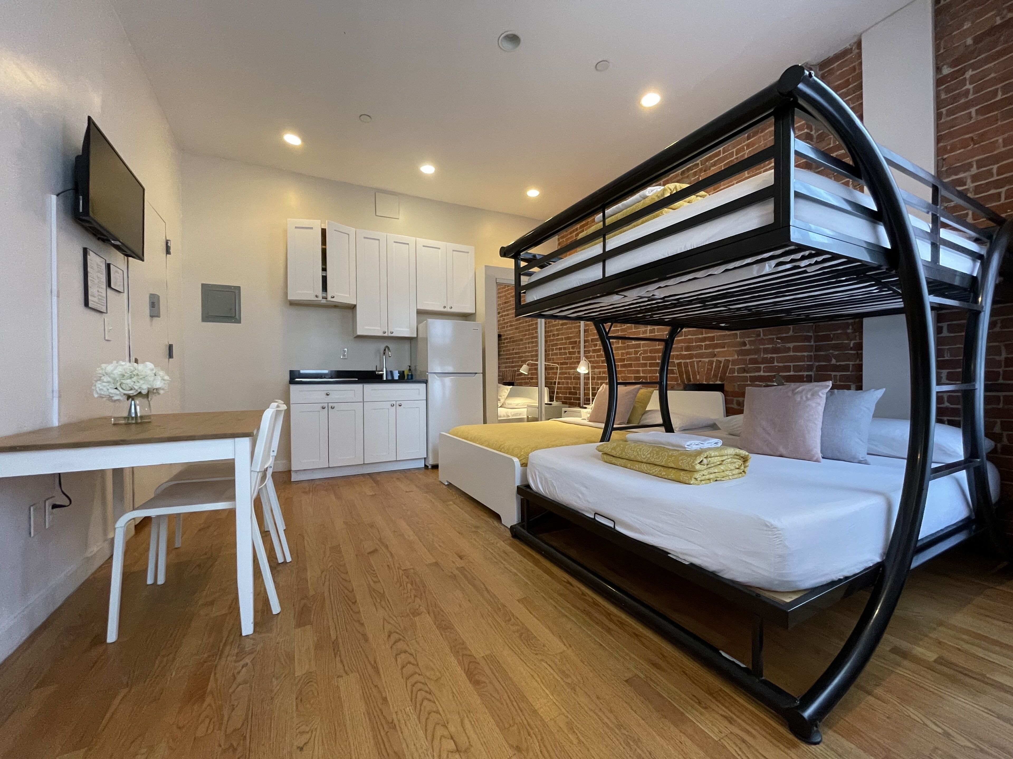 Ein kleines Zimmer mit Etagenbett, einer Küchenzeile, einem Essbereich und einem Fernseher.