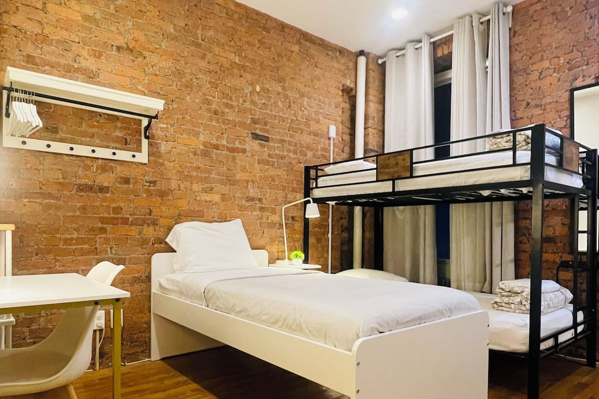 A room with a bunk bed, a desk, and a chair. There is a brick wall and a wooden floor.
