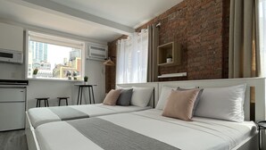 Een moderne slaapkamer met een groot bed, een accentmuur van baksteen en uitzicht op de stad.