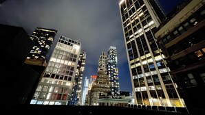 Een nachtelijk stadsbeeld met hoge gebouwen, waarvan sommige verlicht zijn, en een heldere lucht.