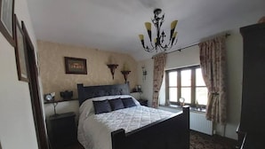 A bedroom with a large bed, a chandelier, a window with curtains, and a radiator. - 2 Bed Flat - Sleeps 3 - Parking - Wifi (Buxton)