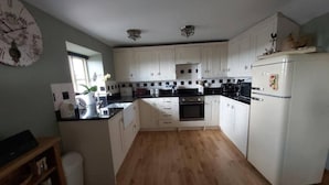 A kitchen with white cabinets, a black countertop, a wooden floor, and a clock on the wall. - 2 Bed Flat - Sleeps 3 - Parking - Wifi (Buxton)
