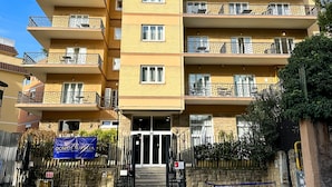 A multi-story residential building with balconies, a gated entrance, and a stone wall.