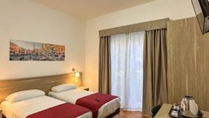 A hotel room with two beds, a desk, a chair, a flat-screen TV, a painting on the wall, and a window with curtains.