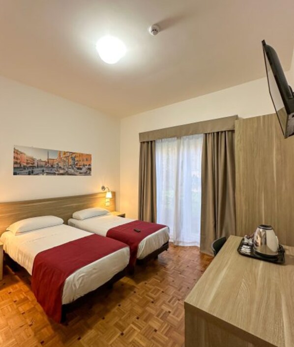 A hotel room with two beds, a desk, a chair, a flat-screen TV, a painting on the wall, and a window with curtains.