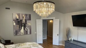 A bedroom with a large bed, a chandelier, a flat-screen TV, and a painting on the wall. - The Belmont - Lux Abode with Pool on Belmont Blvd (Nashville)