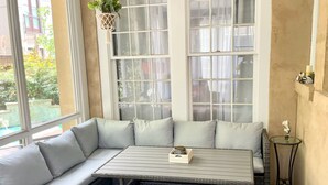 A corner seating area with a cushioned bench and a table, large windows with curtains, and a hanging plant. - The Belmont - Lux Abode with Pool on Belmont Blvd (Nashville)