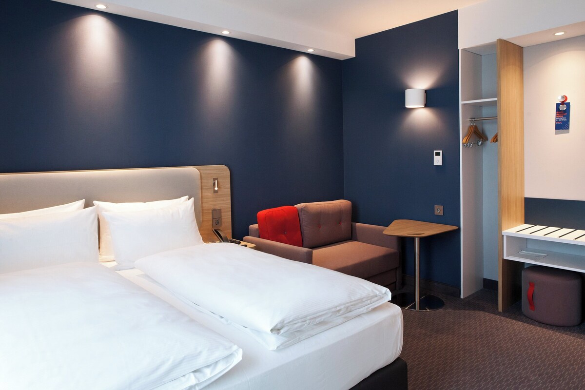 Een hotelkamer met een groot bed, een klein bureau, een stoel en een garderobe.