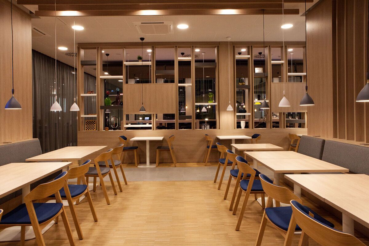 Een modern restaurantinterieur met houten tafels en stoelen, hanglampen en een centraal gelegen zitgedeelte.