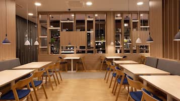 Un interior de restaurante moderno con mesas y sillas de madera, iluminación colgante y una zona de estar central.