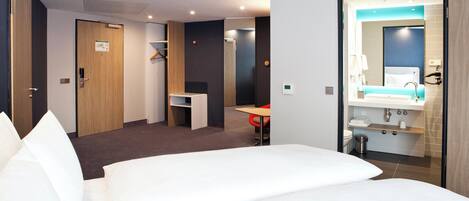 Habitación de hotel con cama, escritorio, silla y baño con lavamanos y espejo.