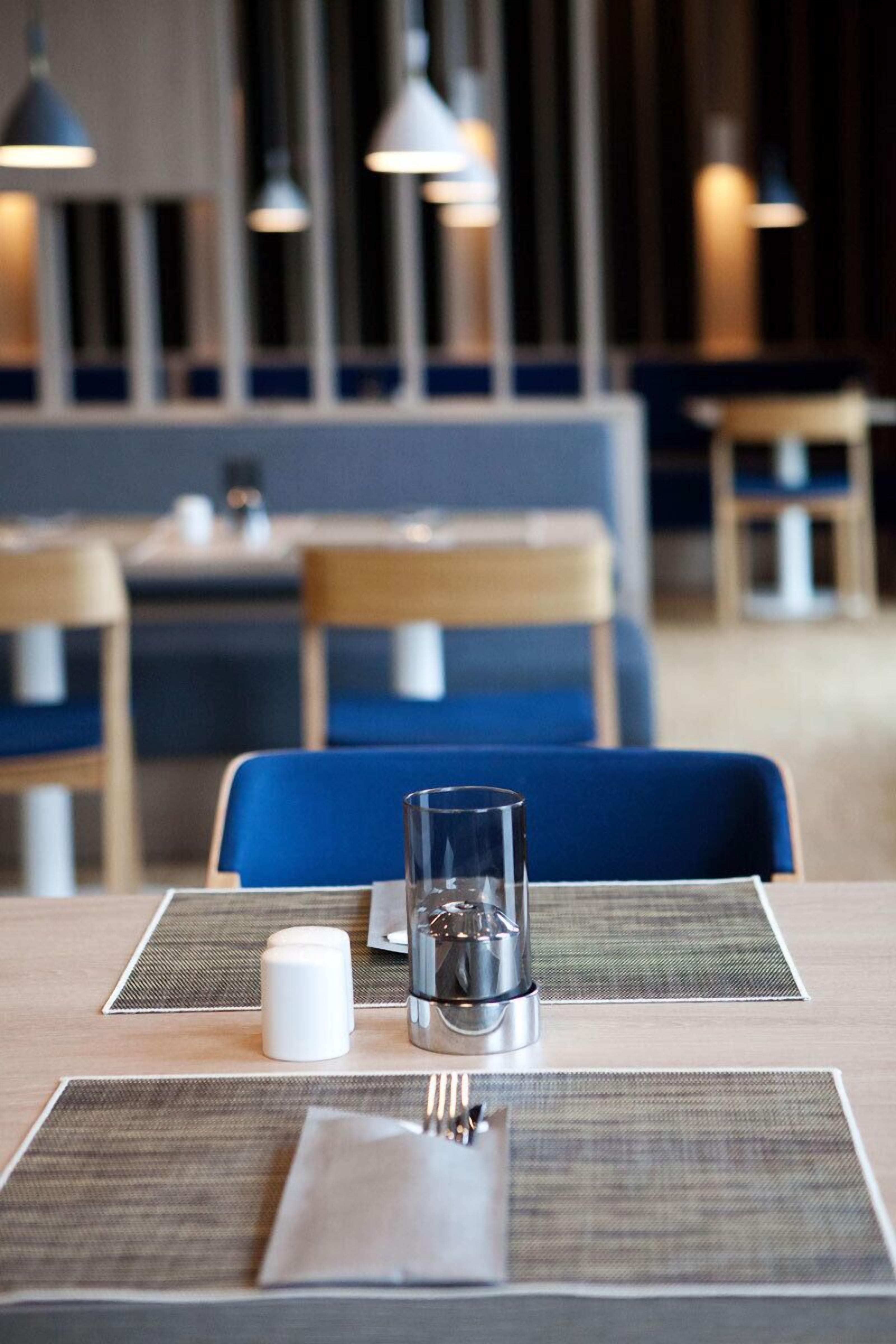 Une table dressée pour deux personnes dans un restaurant, avec un verre, des salières et des poivrières, et une serviette.