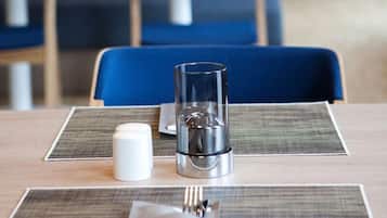 Une table dressée pour deux personnes dans un restaurant, avec un verre, des salières et des poivrières, et une serviette.