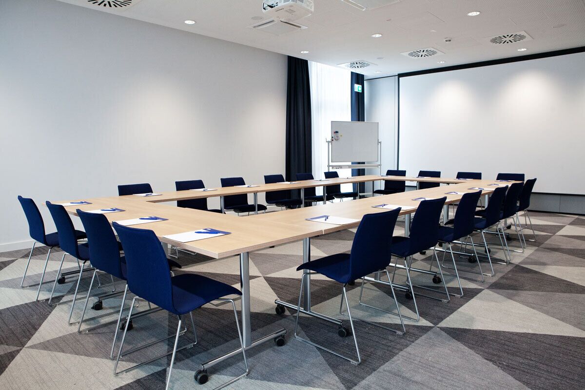 A conference room with a long table, blue chairs, a whiteboard, and a projector screen.