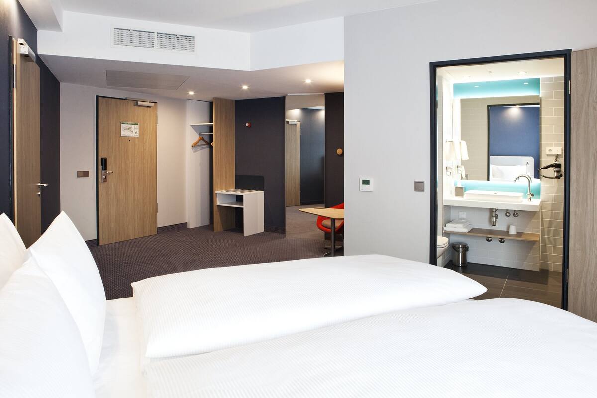 Ett hotellrum med en stor säng, ett skrivbord, en stol, ett litet bord, ett handfat och en spegel.