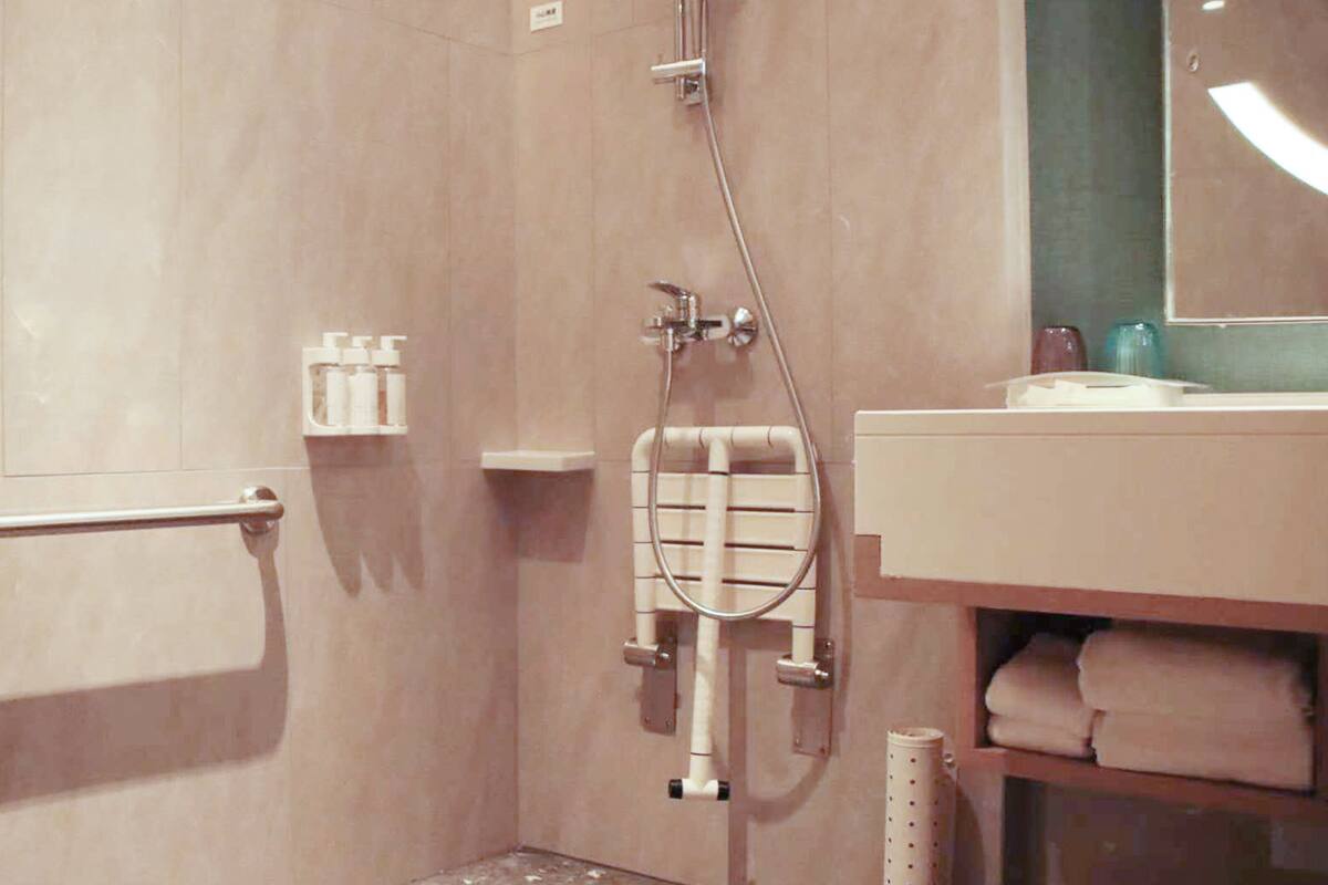 A bathroom with a walk-in shower, grab bars, a towel rack, and a sink with toiletries.