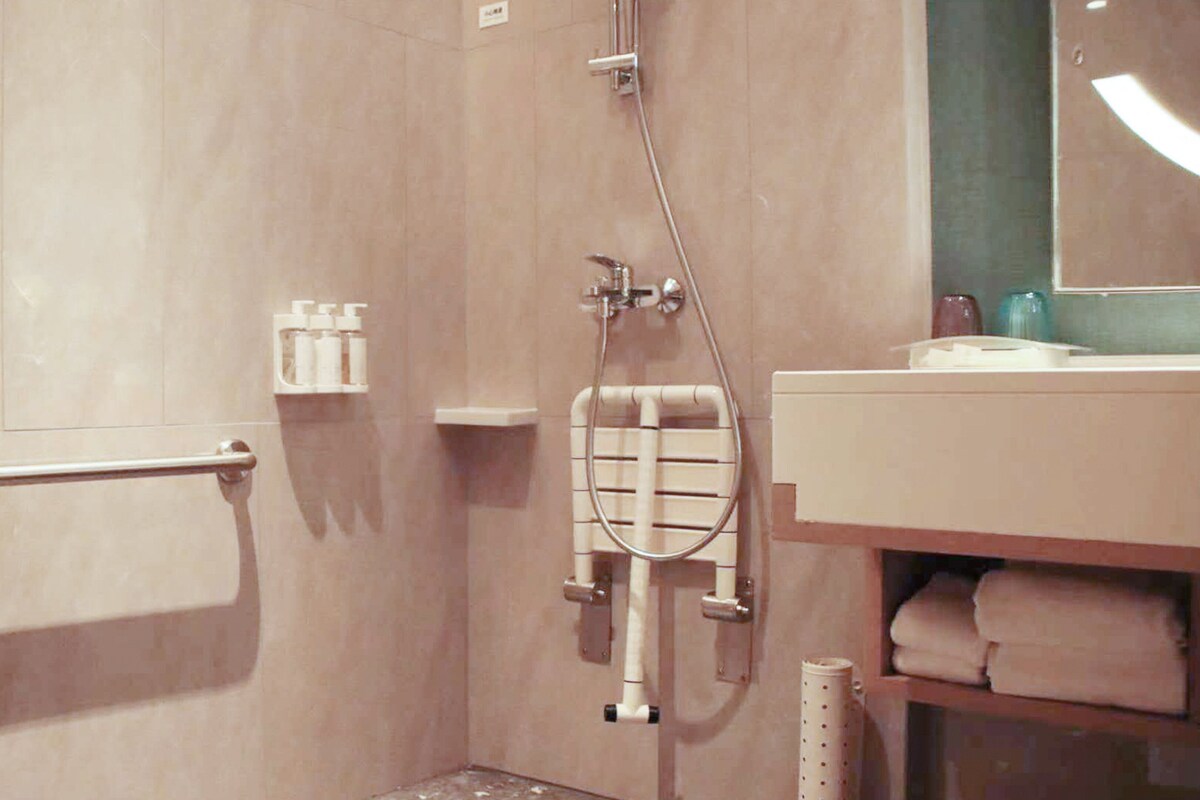 Un baño con ducha a ras de suelo, barras de apoyo, un perchero para toallas y un sujetapapeles.
